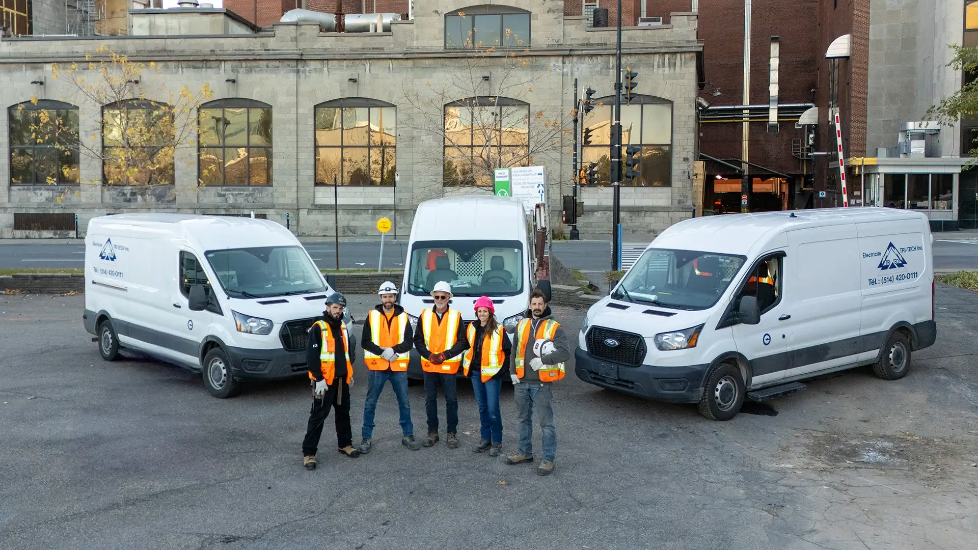 Cinq membres de l’équipe Tri-tech en veste de sécurité devant les véhicules de service de l’entreprise.